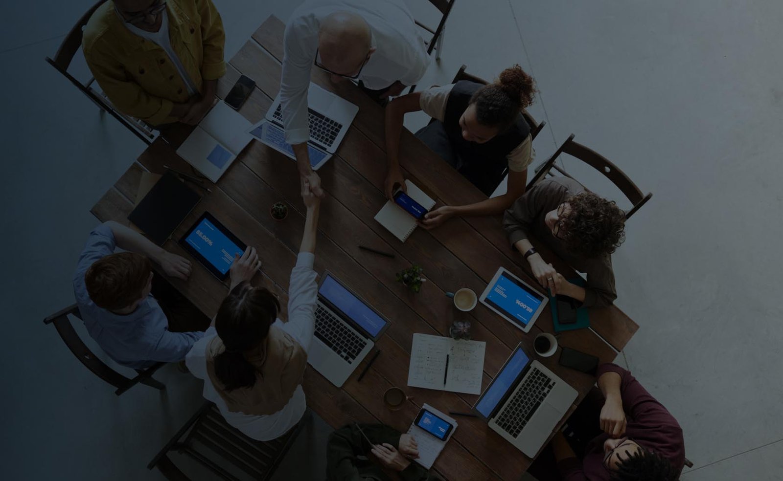 Associates sitting around a meeting table shaking hands.